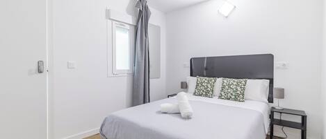 Un dormitorio moderno con una cama grande, una mesita de noche, una lámpara y un ventanal con cortinas.