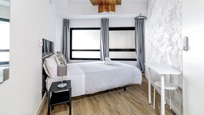 A modern bedroom with a large bed, a bedside table, a small white table, and a wooden ceiling light fixture. - AYZ Princesa - Auto check-in property (Madrid)