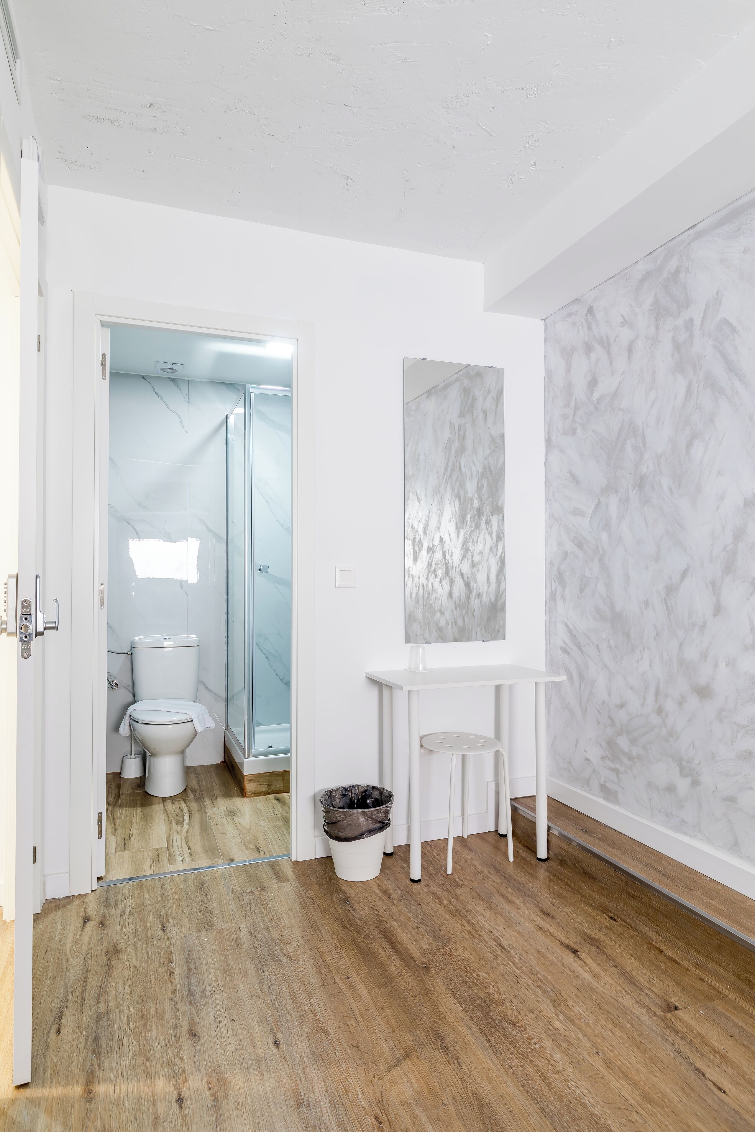 Une salle de bain moderne avec des toilettes blanches, une douche en verre et un mur à l’aspect marbré.