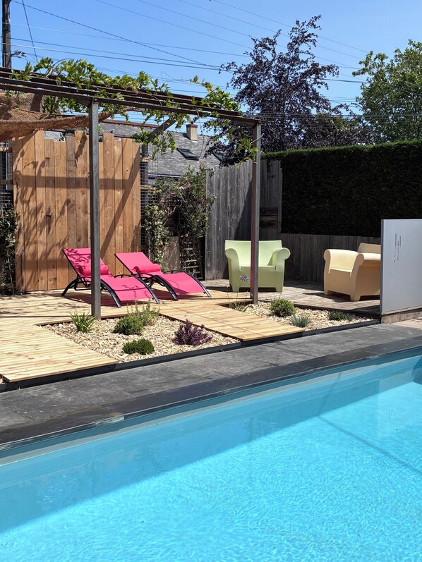 Un jardin avec une piscine, une terrasse en bois et un espace salon extérieur.