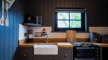 Cocina compacta con horno integrado, cafetera y ventana con vista a zonas verdes.