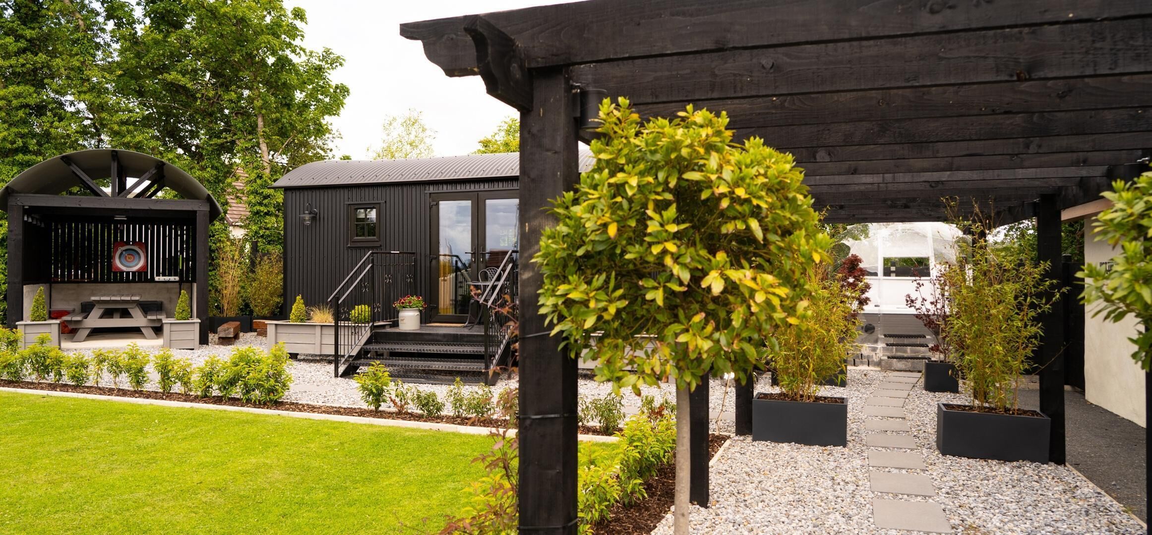 A patio area with a pergola, outdoor seating, and a garden with various plants.