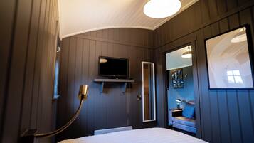 A bedroom with a bed, a mounted TV, a mirror, and a window with a view.