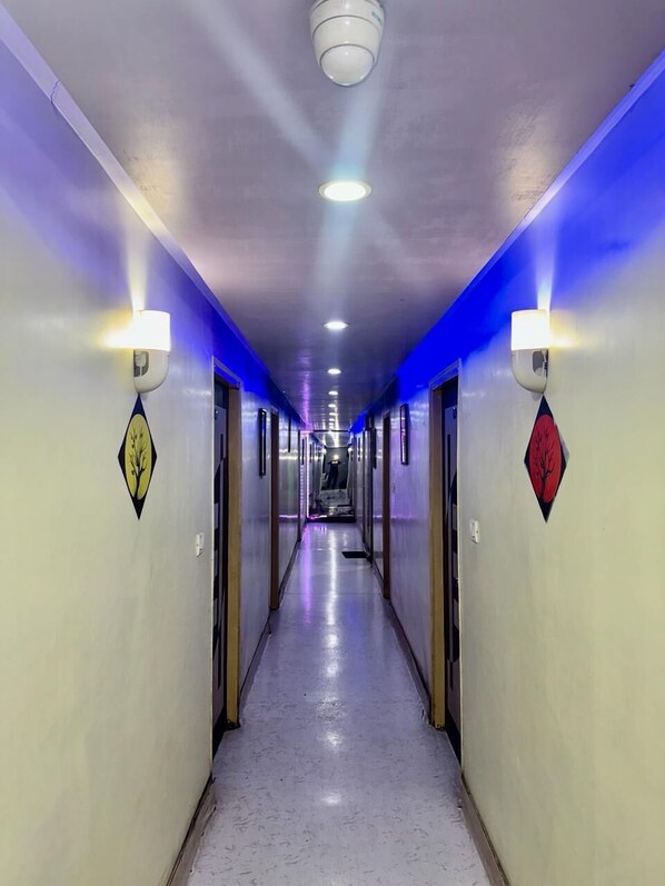 Um corredor comprido e estreito com piso espelhado, ladeado por paredes com arandelas decorativas e obras de arte em formato de diamante.