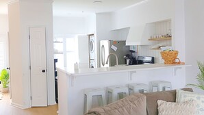 Una cocina moderna con armarios blancos, horno integrado y refrigerador. Hay taburetes de bar y una encimera con una cesta.