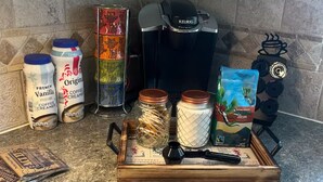Una encimera de cocina con cafeteras, leche para café y una bandeja con cubiertos.