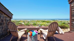 Una terraza de madera con dos sillas Adirondack orientadas hacia la playa.
