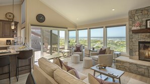 Un amplio salón con chimenea de piedra, grandes ventanales con vistas panorámicas, una cocina equipada con electrodomésticos modernos y una zona de estar acogedora.