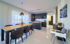 A modern kitchen with a central island, a dining area with a wooden table and chairs, and a small seating area with a high chair.