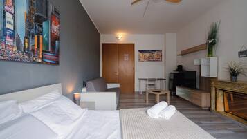 Quarto de hotel moderno com cama, escrivaninha, cadeira, televisão e uma pintura de paisagem urbana.