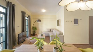 Una sala moderna con un sofá, una mesa de comedor con sillas, un televisor y dos plantas en macetas.