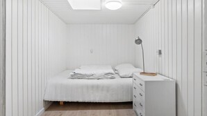 A small, white, single-bed room with a skylight, a bedside lamp, and a white dresser. - 4 bedroom cozy home in Ans By (Ans By)