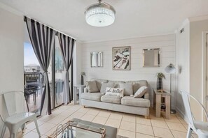 Una sala de estar con un sofá, una mesa de vidrio, una silla, una lámpara y vistas al exterior.