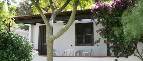 Un edificio blanco con techo de tejas, una ventana con contraventanas y un pequeño patio con mesa y sillas.