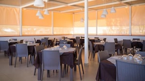 A restaurant with tables set for dining, overhead pendant lighting, and large windows with a view. - Grotta dell' Acqua (Peschici)