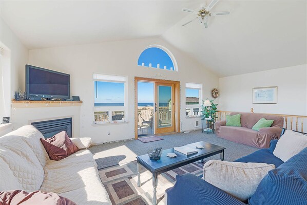 Relax in this spacious living area with a high ceiling and large window offering a view of the outdoors. Enjoy a comfortable seating arrangement with a sofa and couch.