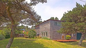 A two-story house with a wooden exterior, a front porch, and a small garden area. - Dragonfly Cabin Westport Wonderful (Grayland)