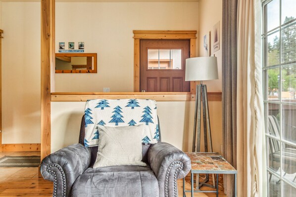 Quarto com poltrona de couro, uma mesinha, luminária, porta de madeira e janela com vista.