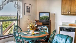 Un coin repas comprenant une table ronde, des chaises, un vase avec des fleurs, un téléviseur et un lave-vaisselle.
