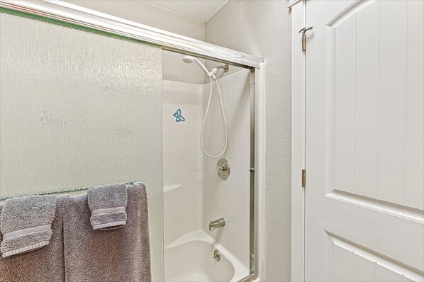 Un baño con ducha, un perchero con toallas y una puerta.
