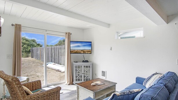 A living room with a sofa, a coffee table, and a television. There is a sliding glass door leading to an outdoor area.