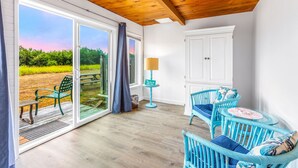 A room with a wooden ceiling, a view of a field through large windows, a white cabinet, and blue wicker furniture. - Waters Edge Condo in Ocean Shores (Ocean Shores)