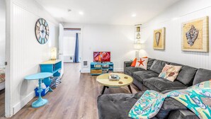 A modern living room with a grey sofa, a round coffee table, and a blue side table. There is a large wall clock and artwork on the walls. - Waters Edge Condo in Ocean Shores (Ocean Shores)