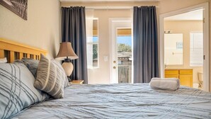 A bedroom with a bed, a nightstand, a lamp, and a view of the outside. - Comfortable 3BR townhouse w/ pvt patio (Davenport)