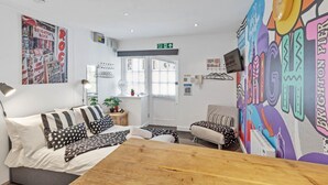 A modern hotel room with a bed, a wooden table, a sofa, and a colorful mural.