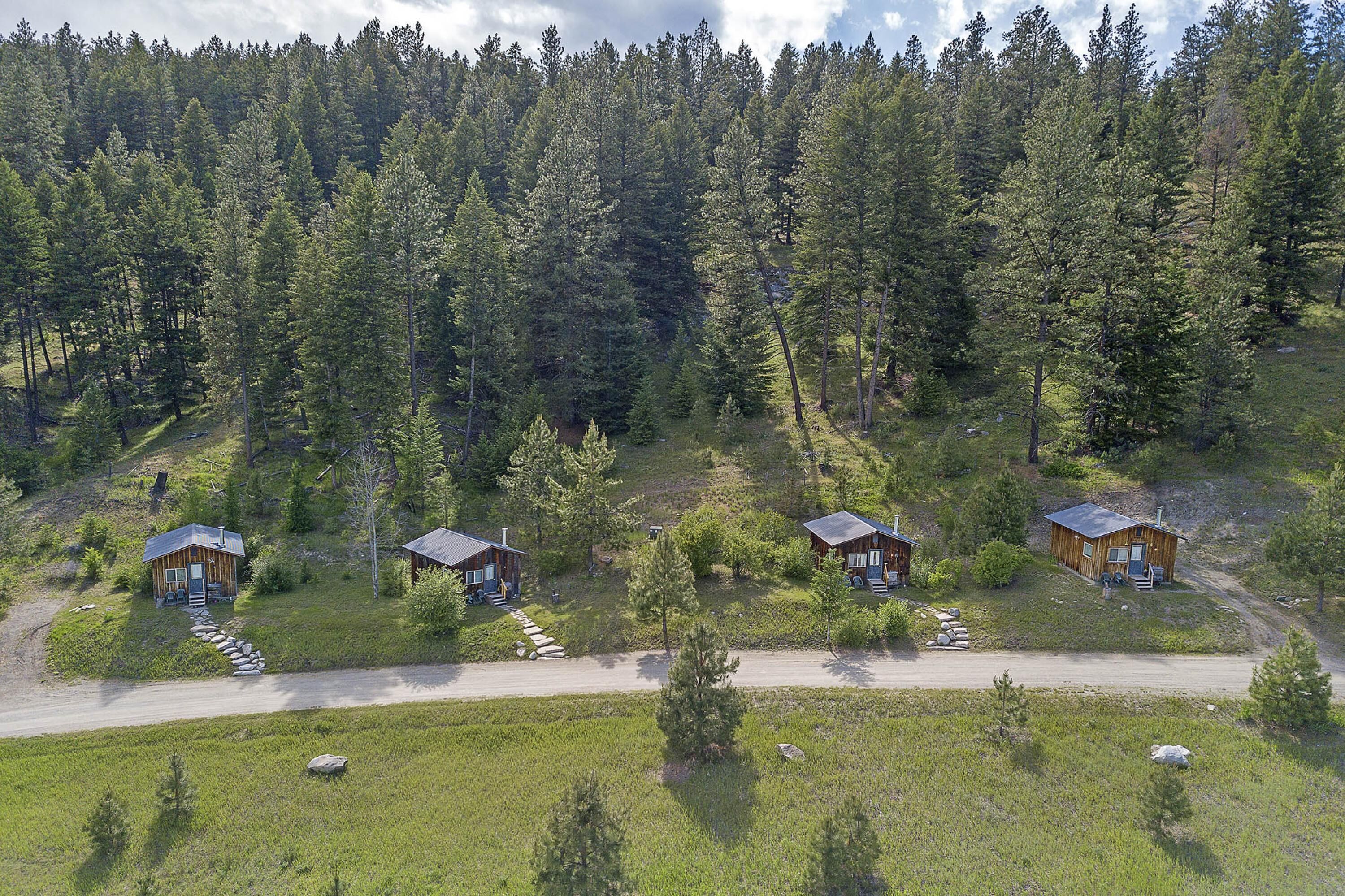 A remote cabin area with four wooden cabins, surrounded by dense forest, accessible by a dirt road.