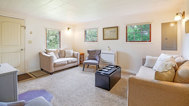 A living room with a beige sofa, a grey armchair, and a coffee table. There are two windows with views of greenery. - Crabbin Cabin Westport (Westport)
