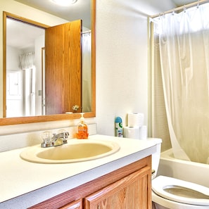 A bathroom with a wooden vanity, a sink, a mirror, a toilet, and a shower curtain.