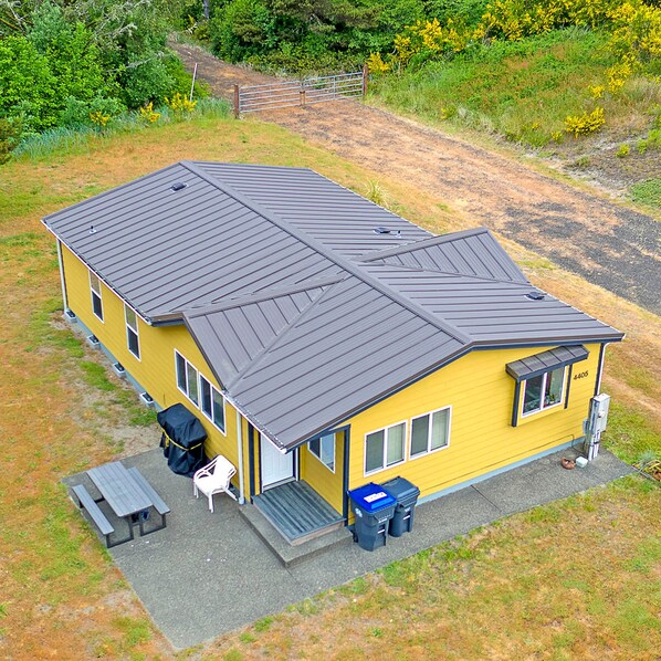 Een geel huis met één verdieping, een donker dak, een overdekte patio en een klein zitgedeelte buiten.