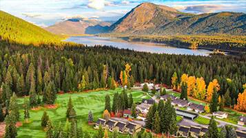 A residential area with houses, a golf course, and a lake surrounded by mountains.
