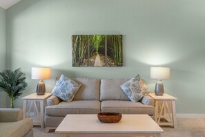 Ein Wohnzimmer mit einer Couch, zwei Beistelltischen mit Lampen, einem Couchtisch und einem an der Wand hängenden Bild von einem Pfad durch einen Bambushain.