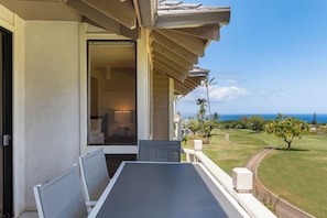 Un balcon avec une table et des chaises, donnant sur un terrain de golf et l’océan.