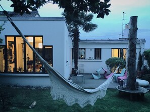 Een modern huis met een hangmat in de tuin, een boom en een stoel.