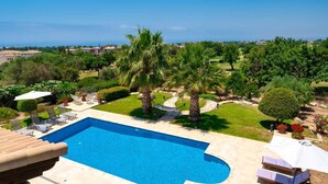 A swimming pool with a curved edge, surrounded by palm trees and a well-maintained lawn. - Villa 148 - Lofou in Kouklia (Kouklia)