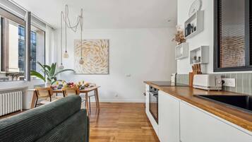 A modern kitchen with wooden flooring, white cabinetry, and a dining area with a table and chairs.