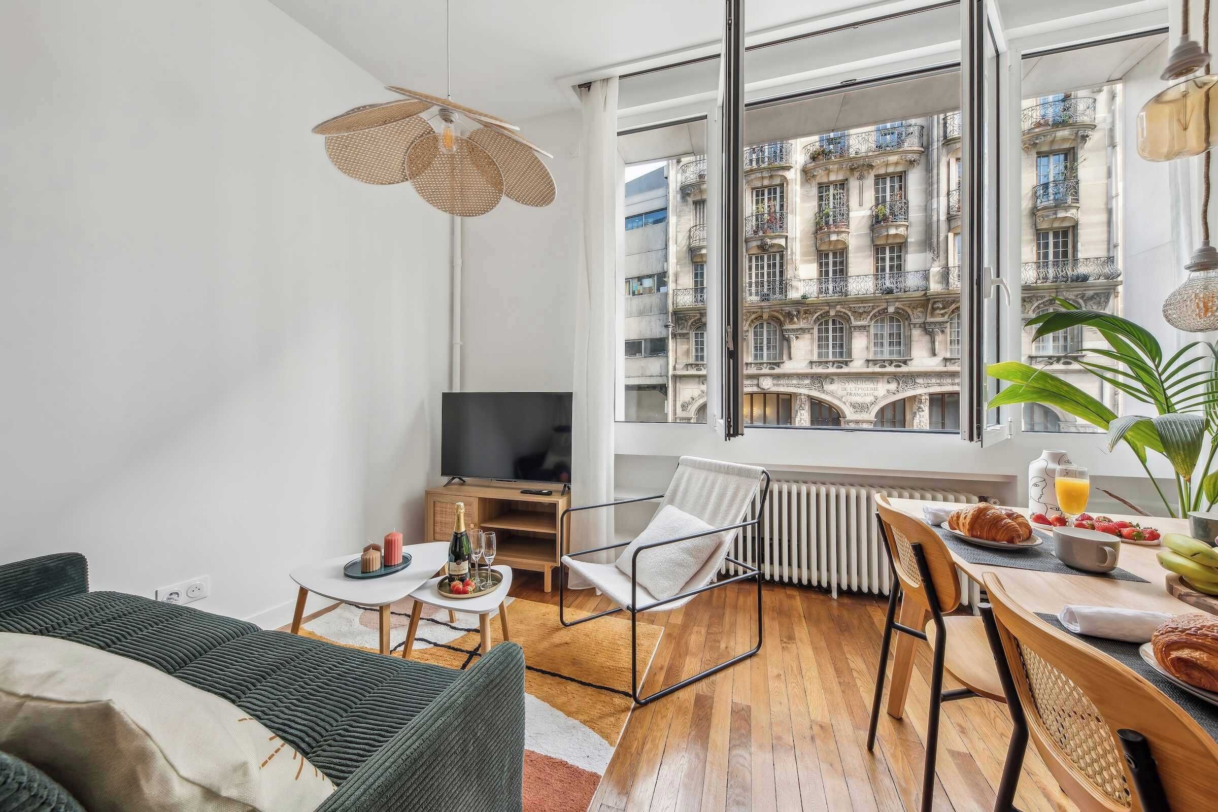 A modern living room with a sofa, a dining table with breakfast items, a TV, and a large window with a city view.