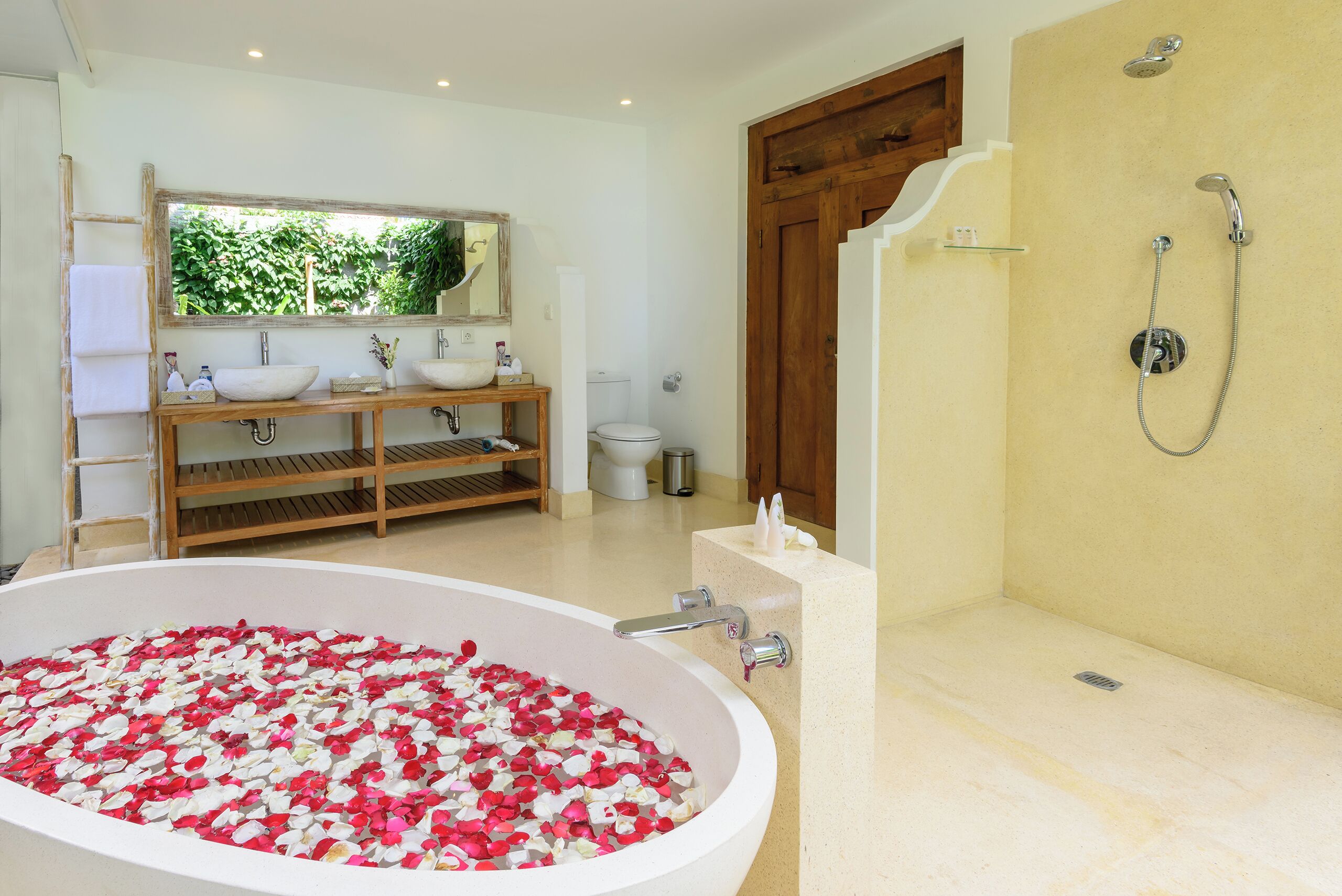 A bathroom with a large bathtub filled with rose petals, a wooden vanity with two sinks, and a shower area.