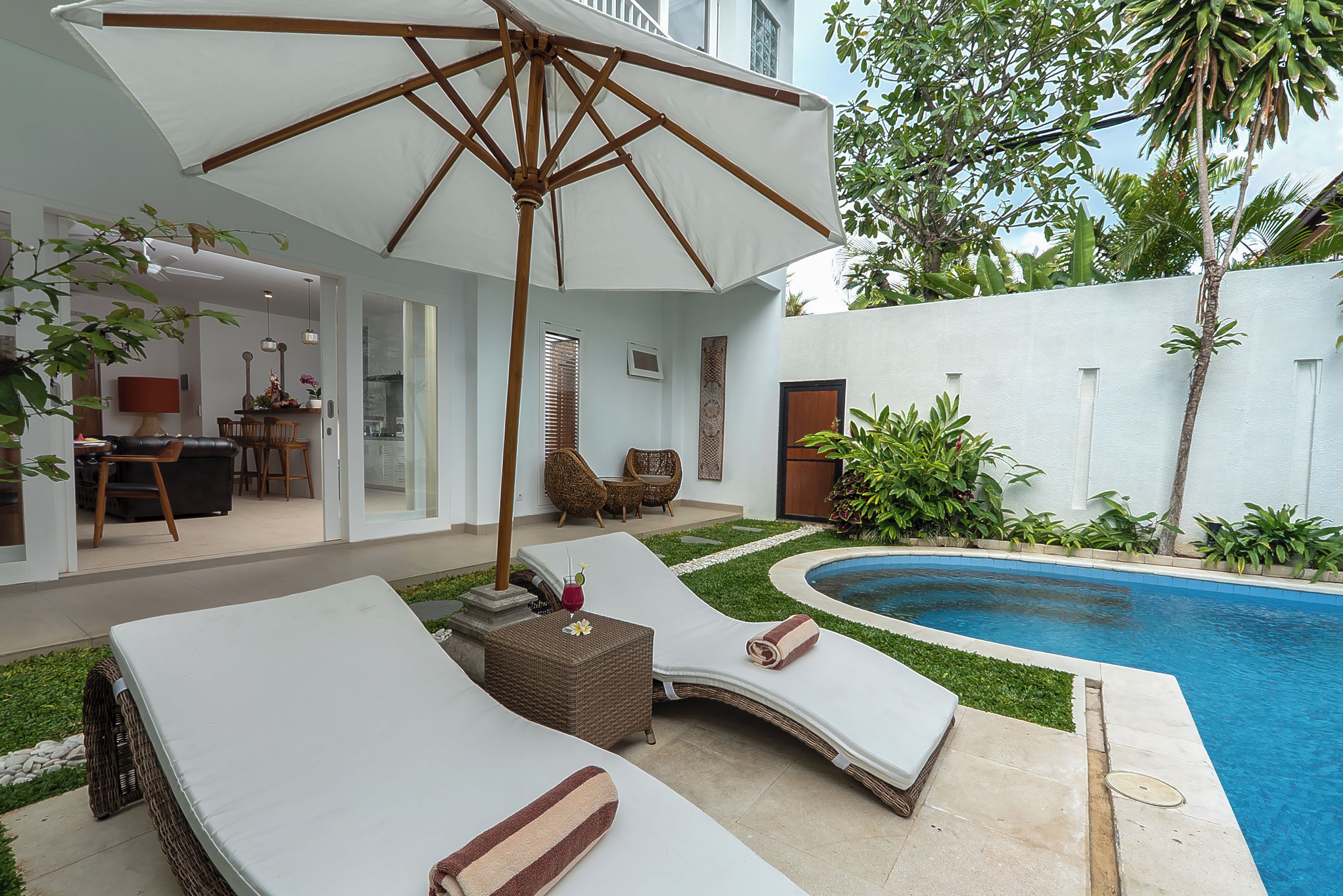 Área de piscina com espreguiçadeiras, uma mesa e um grande guarda-sol.
