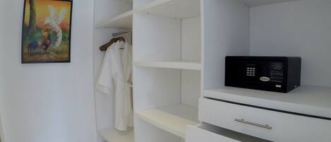 A walk-in closet with white shelves and drawers, a black microwave on the top shelf, and a painting of a bird on the wall.