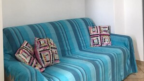 Ein Zimmer mit einem blau gestreiften Sofa, zwei gemusterten Kissen, einer weißen Wand und einem Regal mit Dekoration.