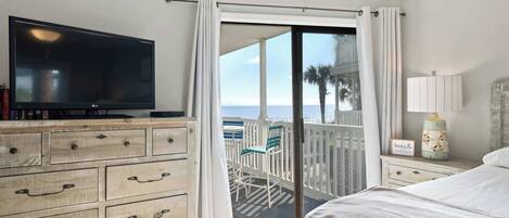 A bedroom with a TV, wooden dresser, and a balcony with a view of the beach.