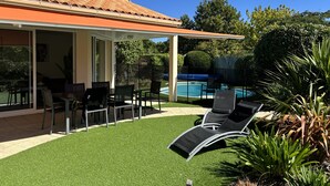 Ein überdachter Patio-Bereich mit Gartenmöbeln, einem Schwimmbad und einem gepflegten Rasen.
