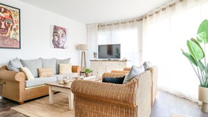 Ein Wohnzimmer mit Rattanmöbeln, einem Flachbildfernseher und Bildern an den Wänden.