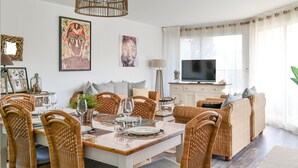 Ein modernes Wohnzimmer mit Essbereich, Korbmöbeln und Kunstwerken an den Wänden.