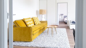 Una sala de estar moderna con un sofá amarillo mostaza, cojines estampados, una lámpara blanca y una pequeña mesa redonda.
