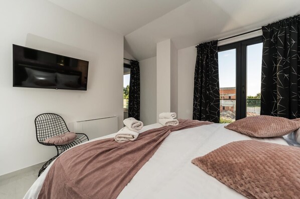 A modern hotel room with a large bed, a flat-screen TV, a chair, and a view of the outside. - Villa Antea Dalmacija ZadarVillas (Privlaka)
